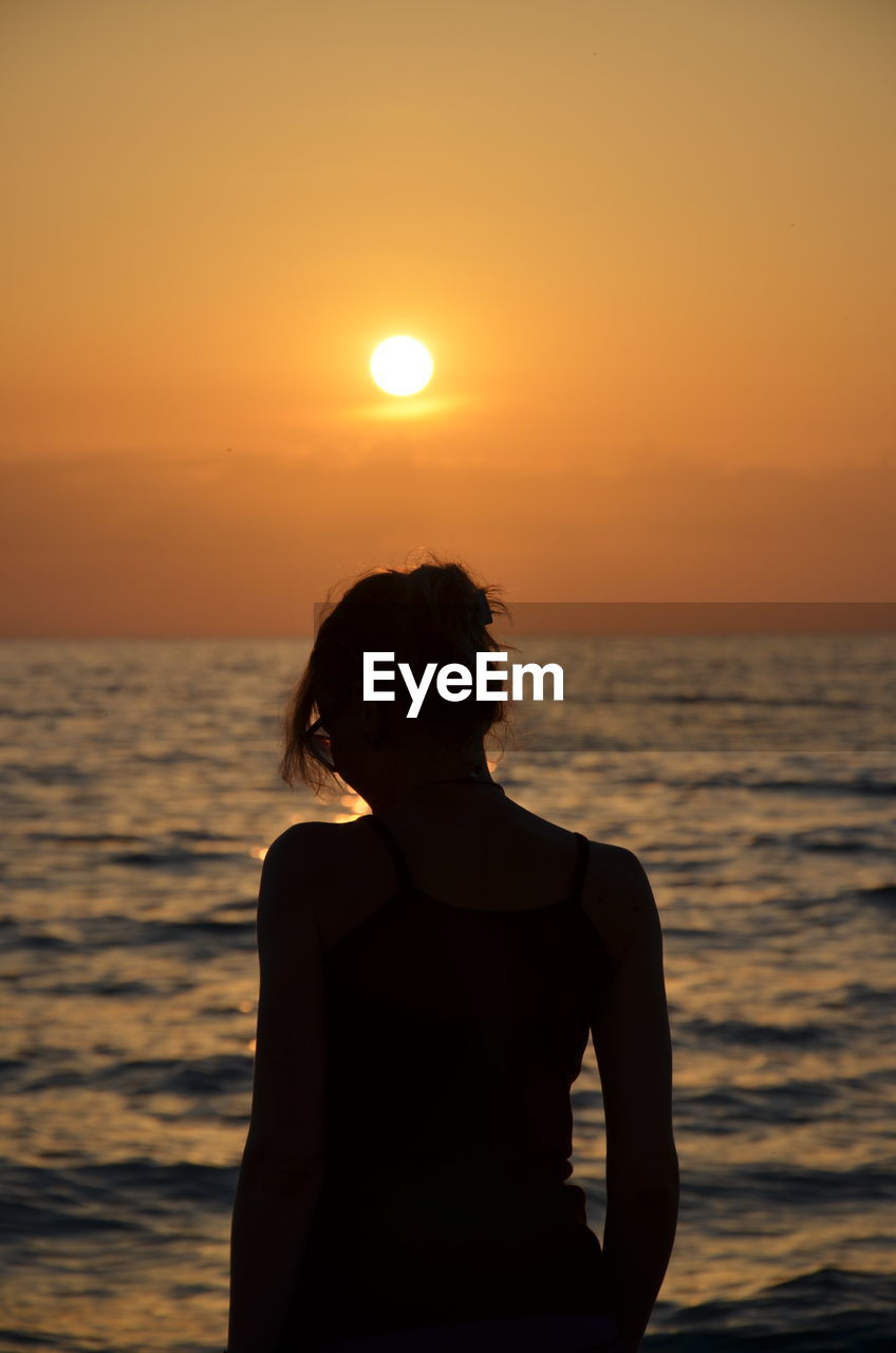 Rear view of woman looking at sea during sunset