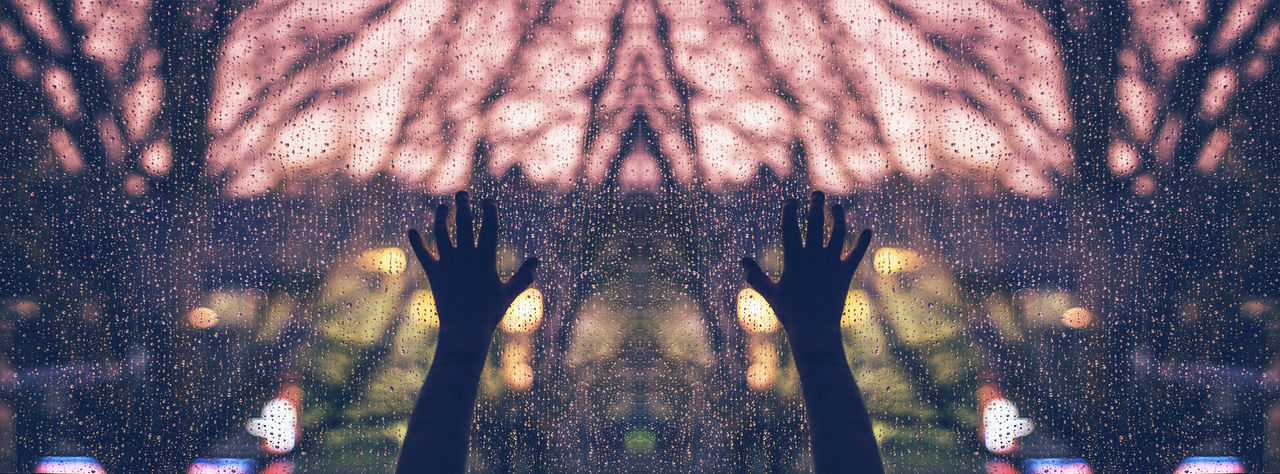 Cropped image of hand on wet glass window on rainy day