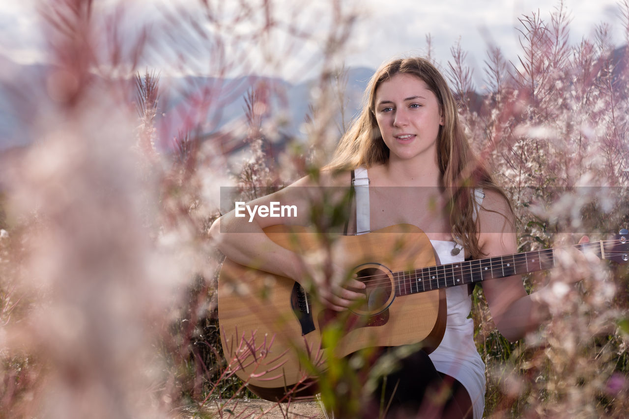 Young woman playing guitar while sitting amidst flowering plants on field