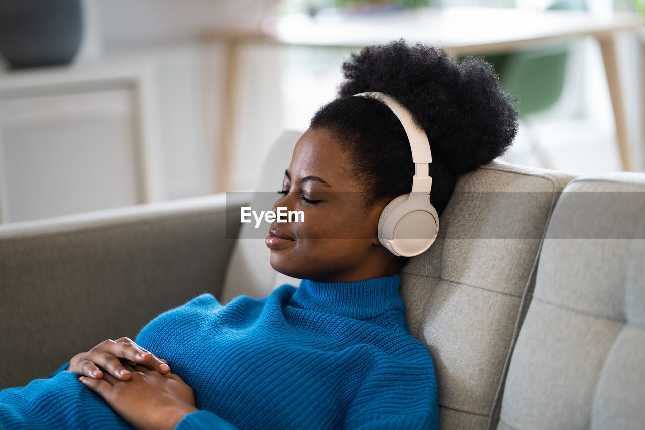 Calm african american woman listening to music in wireless headphones lying with closed eyes