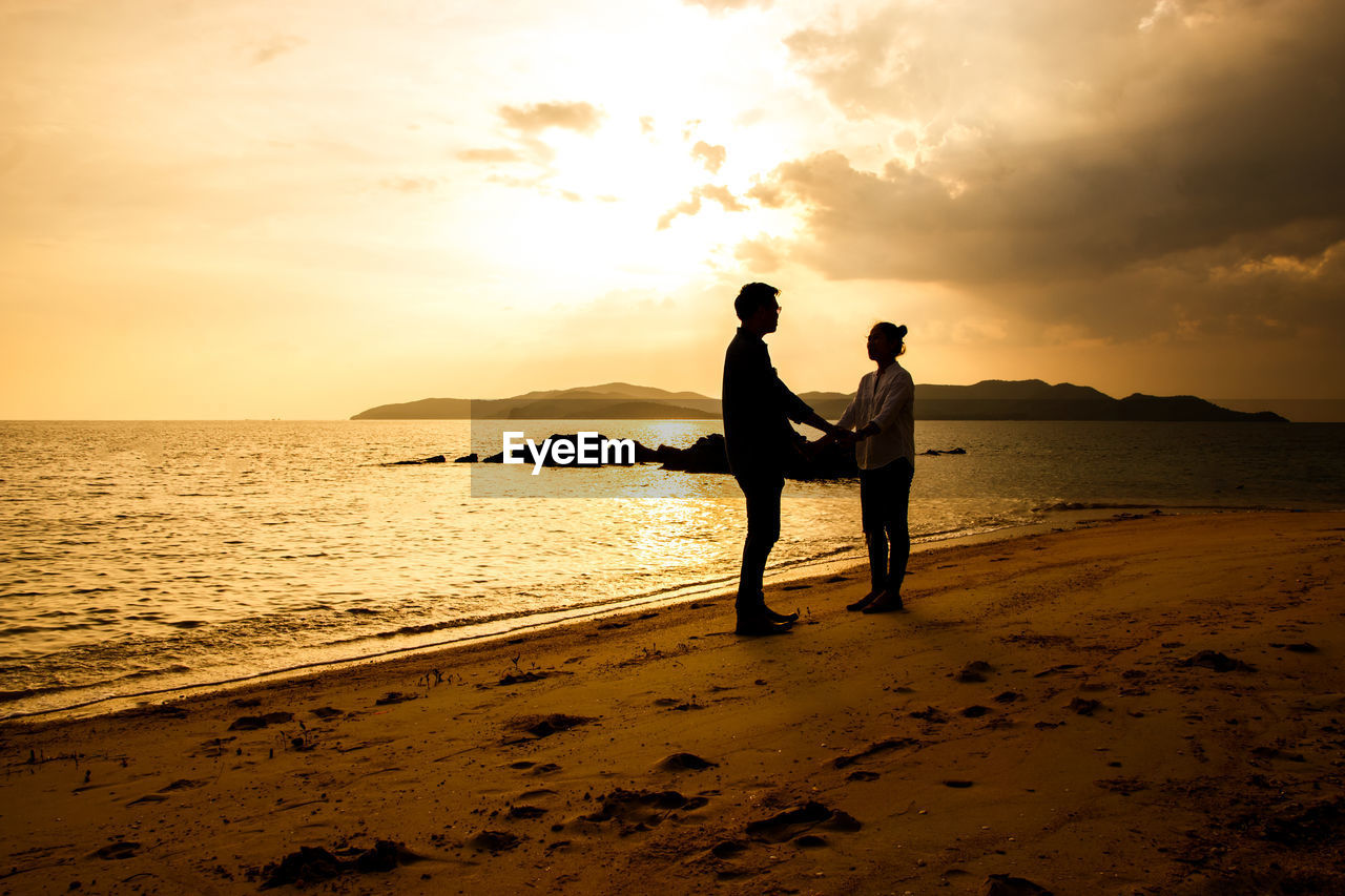 SILHOUETTE FRIENDS ON BEACH AGAINST SKY DURING SUNSET