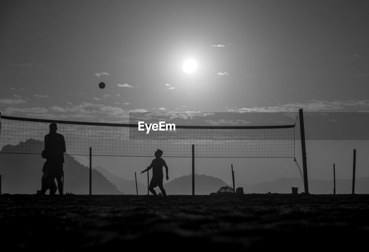 PEOPLE PLAYING SOCCER ON BEACH AGAINST SKY