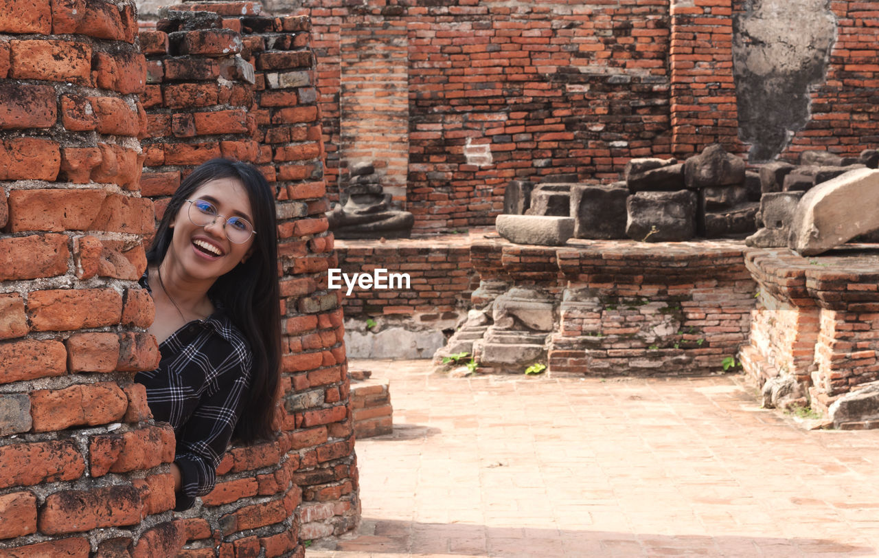 Portrait of smiling young woman against brick wall