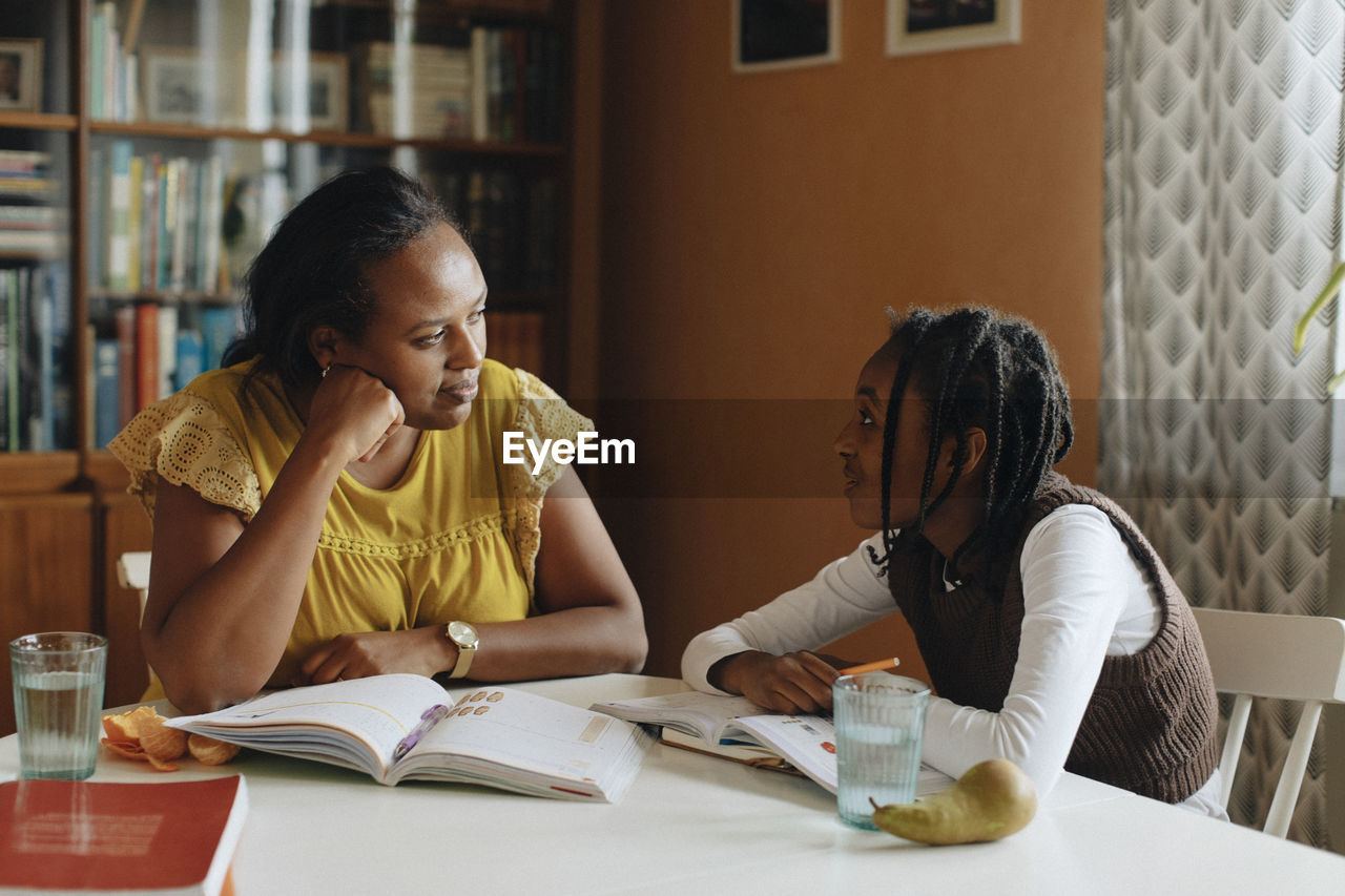 Mother and daughter talking to each other while studying at home