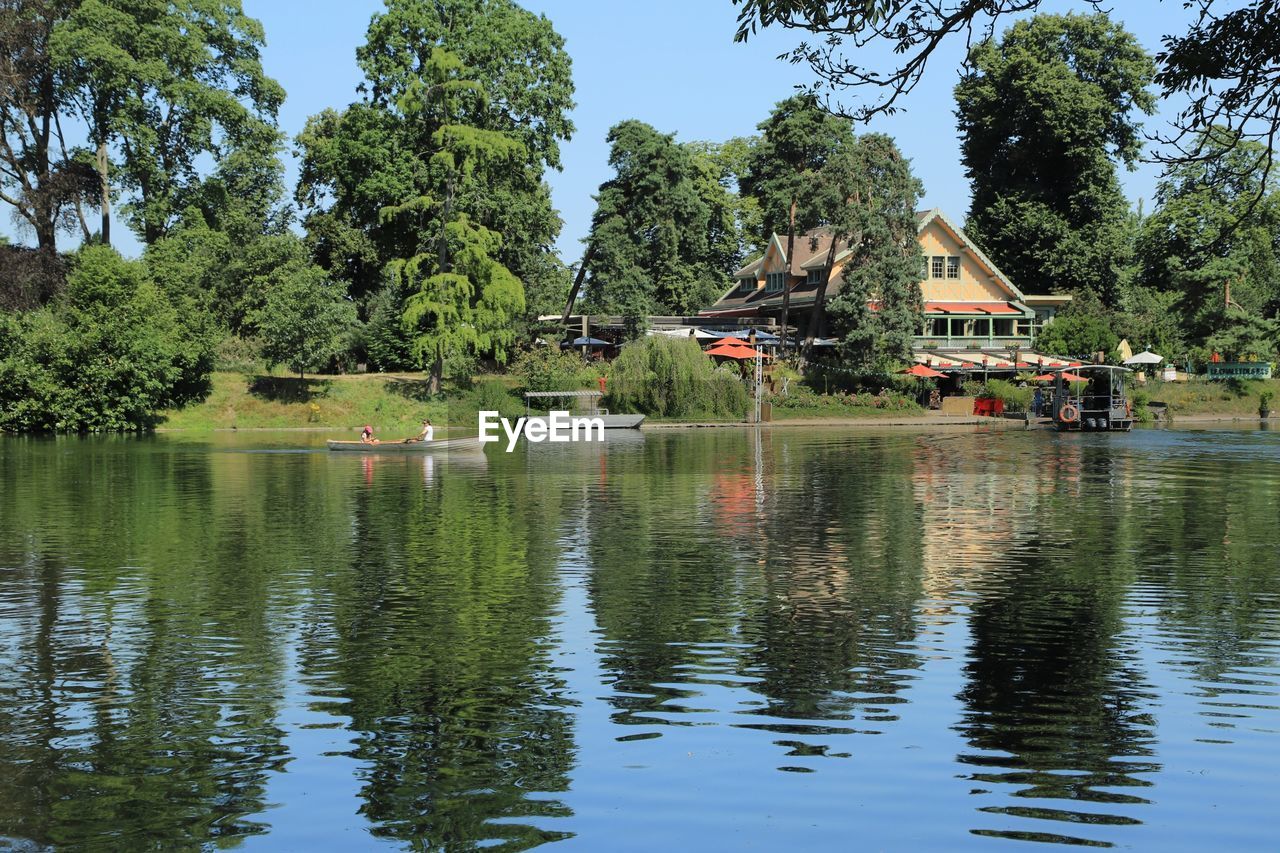 SCENIC VIEW OF LAKE BY TREES AND BUILDINGS