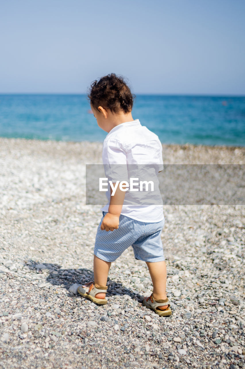 Happy toddler boy in white shirt and blue shorts on the beach