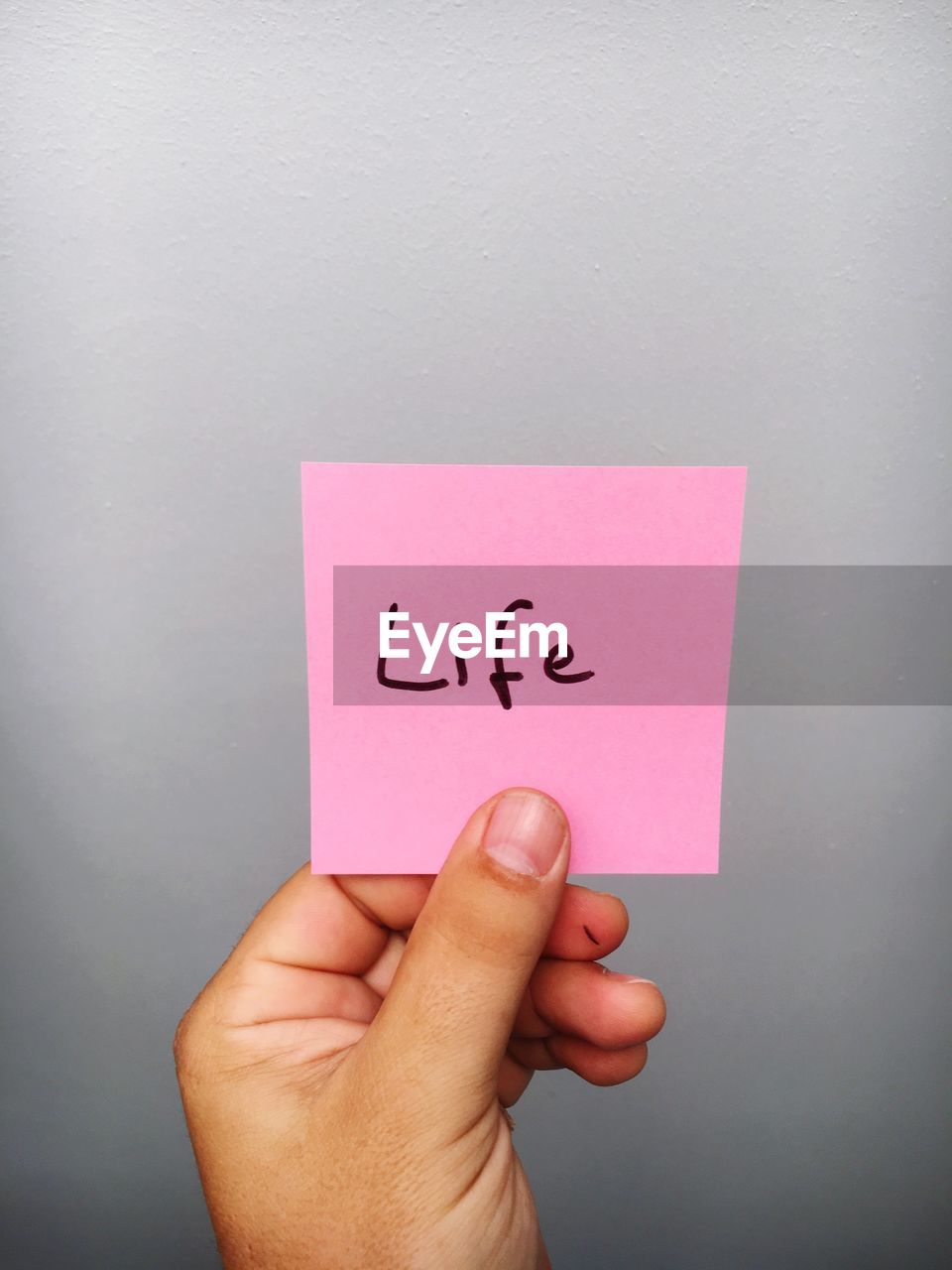 Cropped hand of person holding life text on adhesive note against gray background