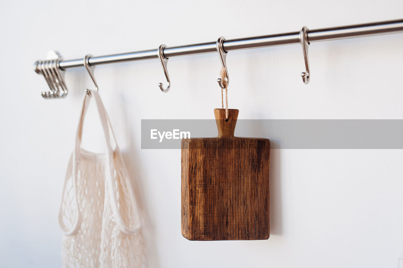 A dark wood cutting board hangs on a hook in the white kitchen, isolated next to knitted string bag