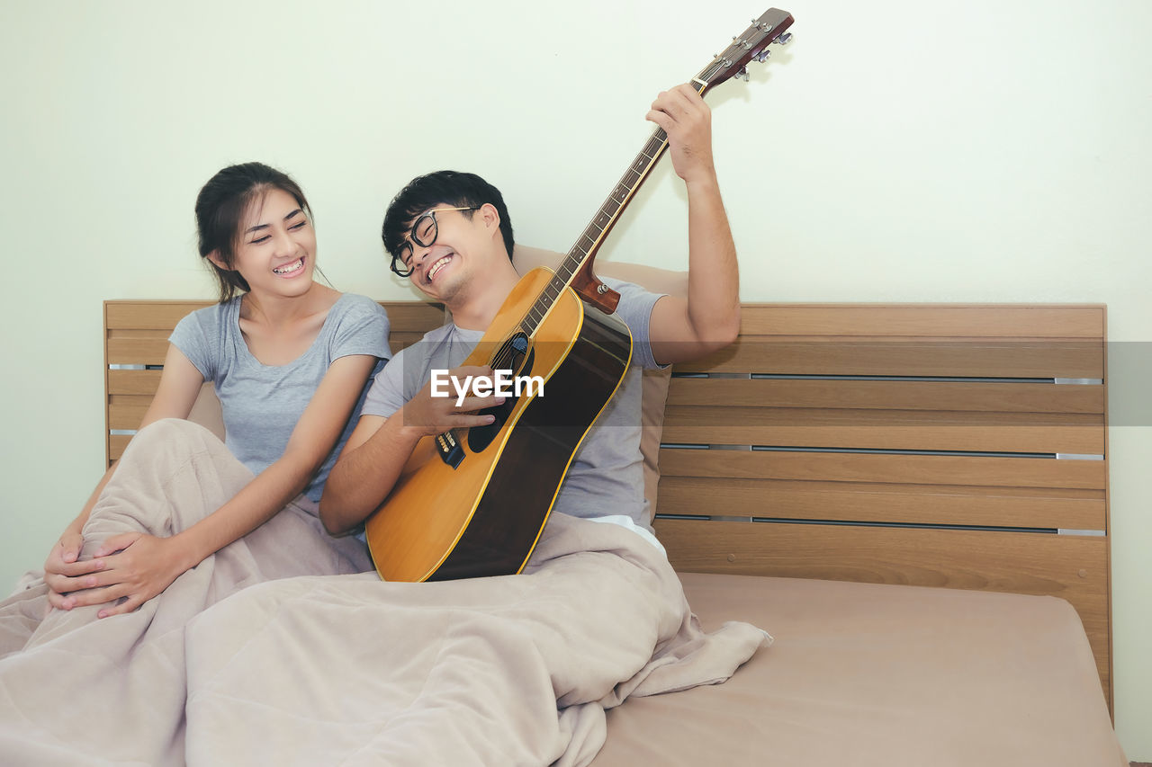 Close-up of man playing guitar with girlfriend at home