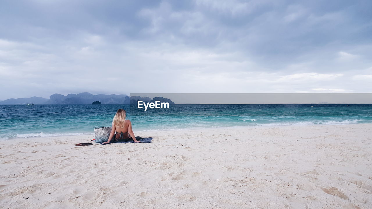 Rear view of woman sitting on beach against sky