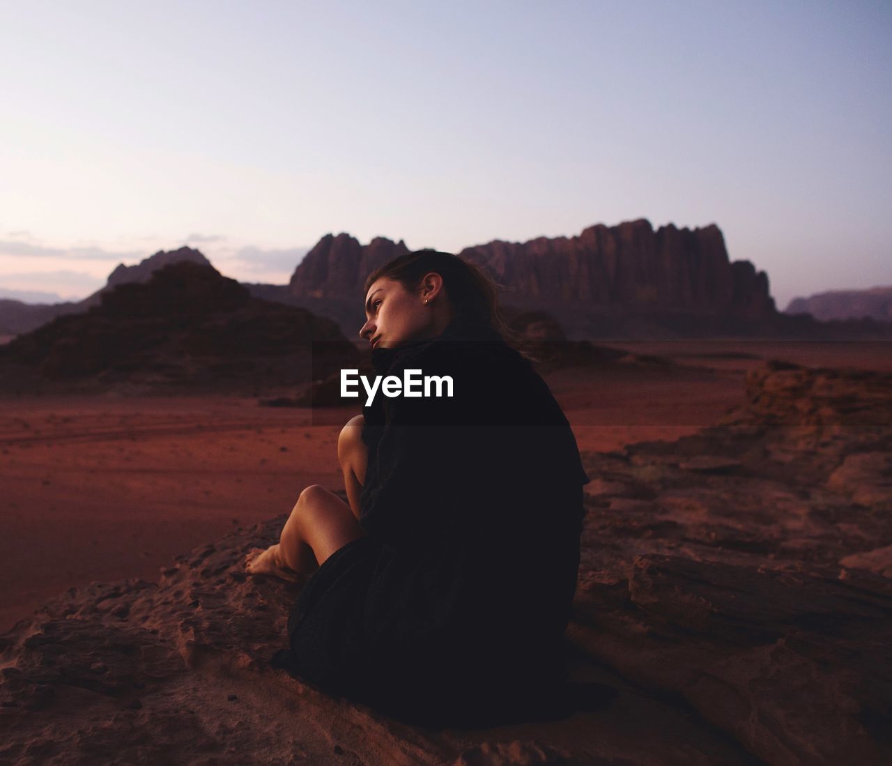 Woman sitting on rock in desert against clear sky