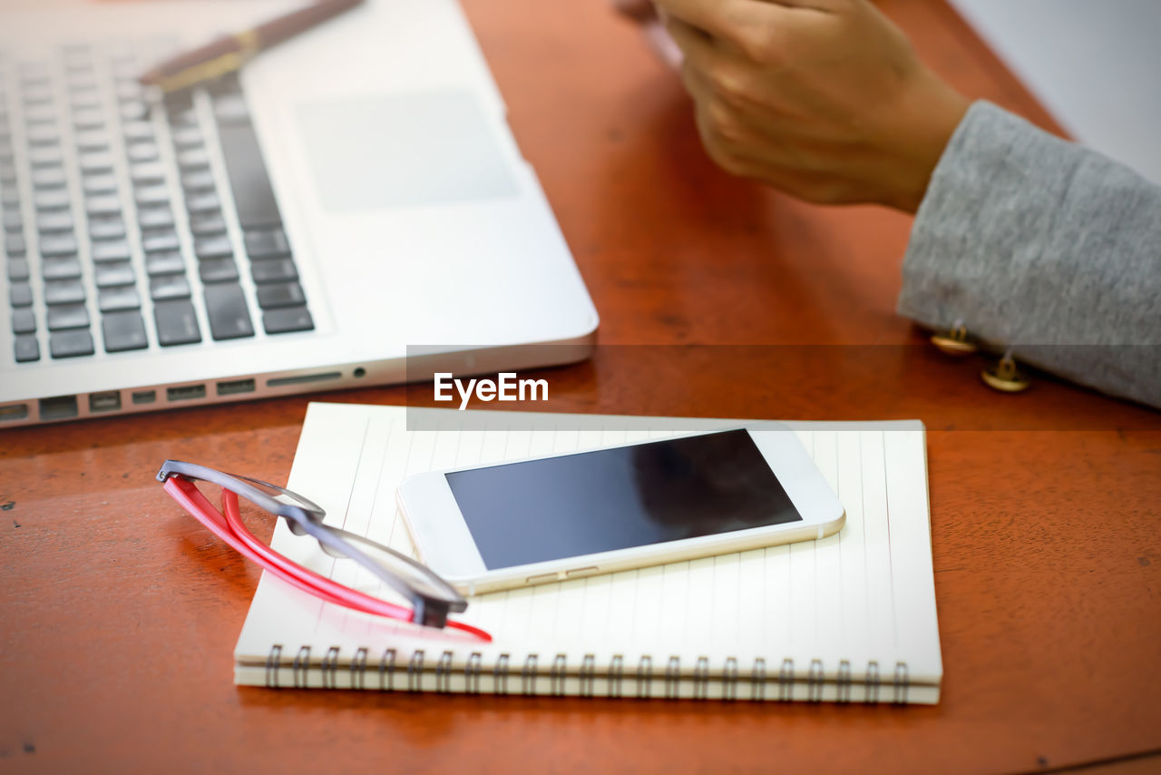 Cropped image of businesswoman with mobile phone and diary on desk