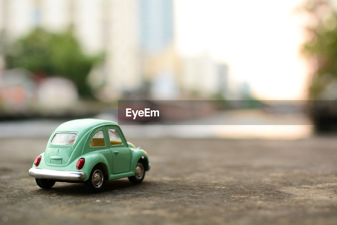 CLOSE-UP OF TOY CAR ON ROAD IN CITY