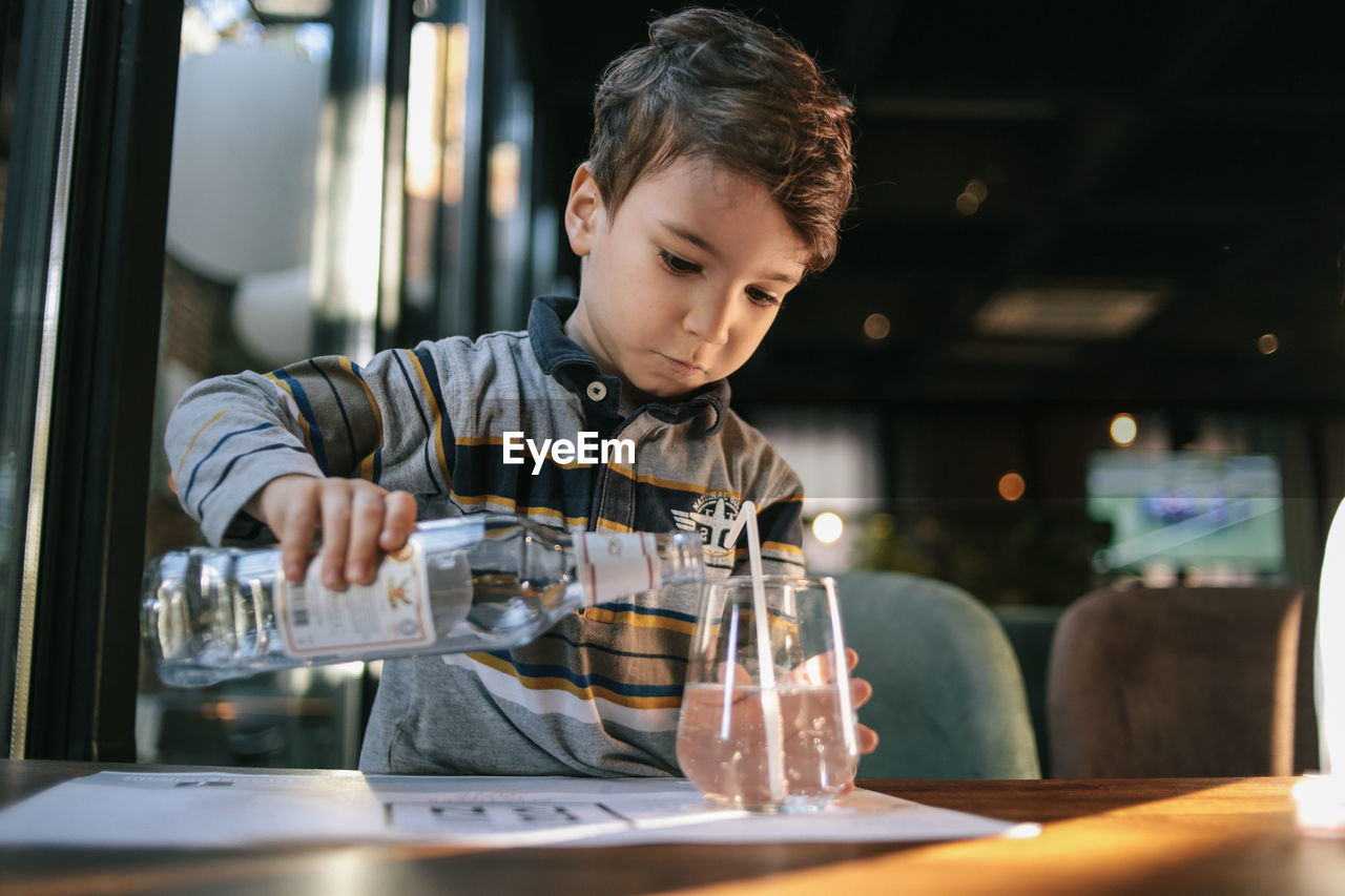 A little boy pours himself a glass of water from a bottle in a cafe. independence and maturity. 