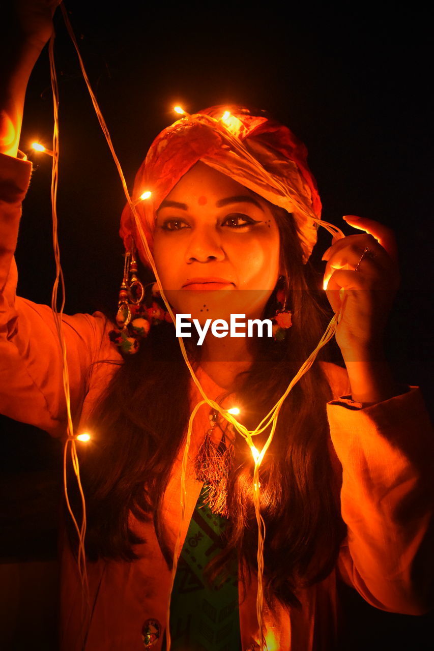 Woman looking at illuminated string light against black background