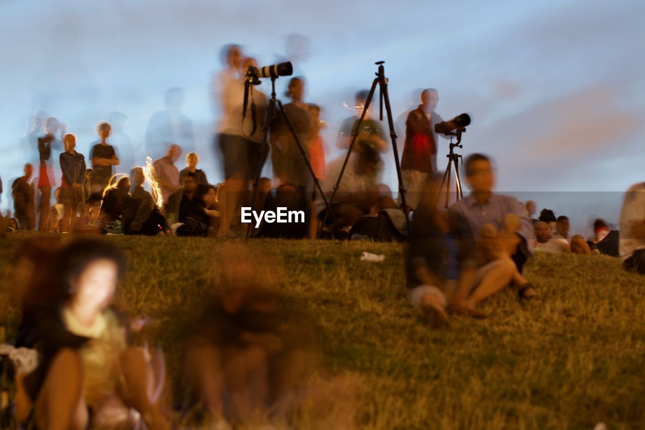 GROUP OF PEOPLE SITTING ON FIELD BY LAND AGAINST SKY