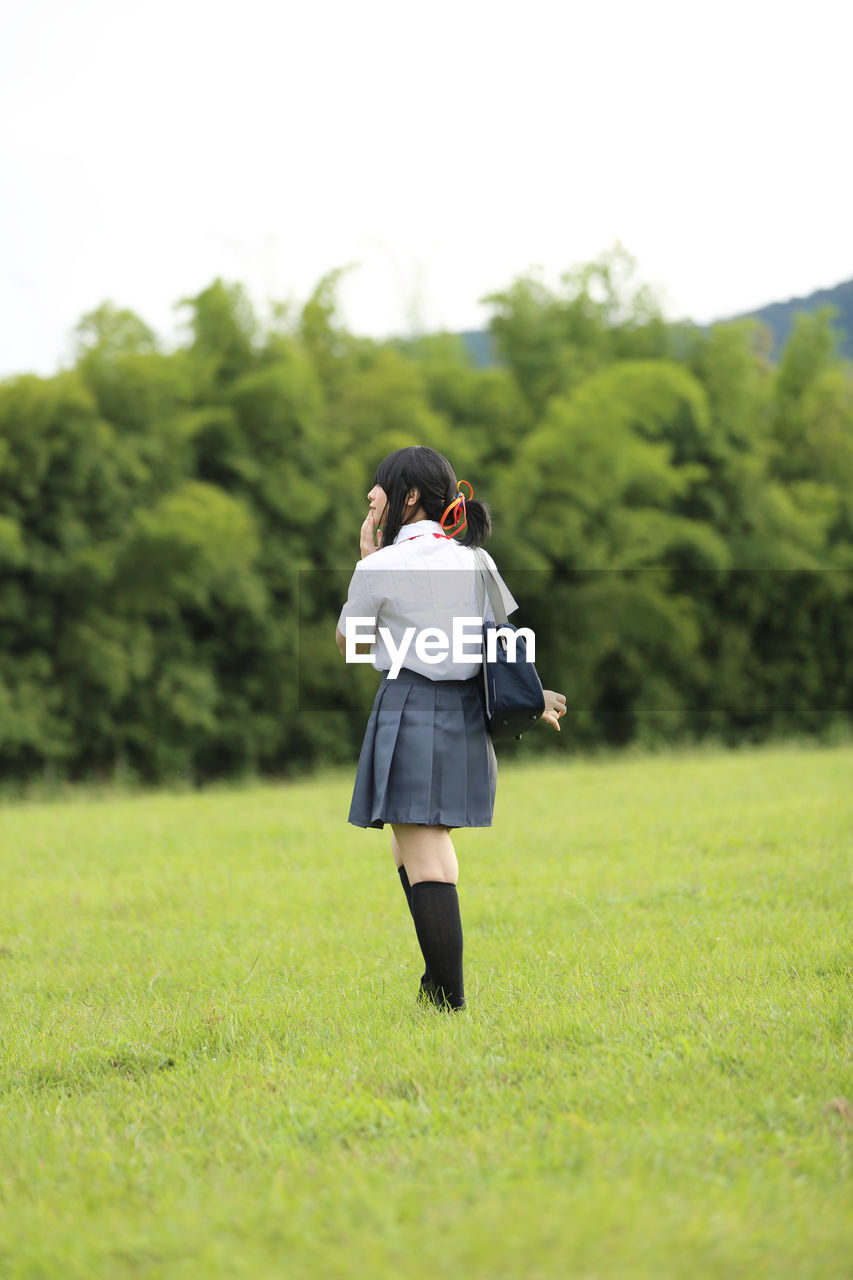 Rear view of woman in school uniform walking on field