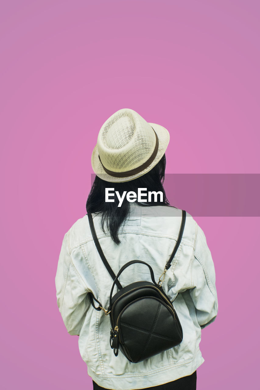 REAR VIEW OF WOMAN STANDING BY PINK HAT AGAINST GRAY BACKGROUND