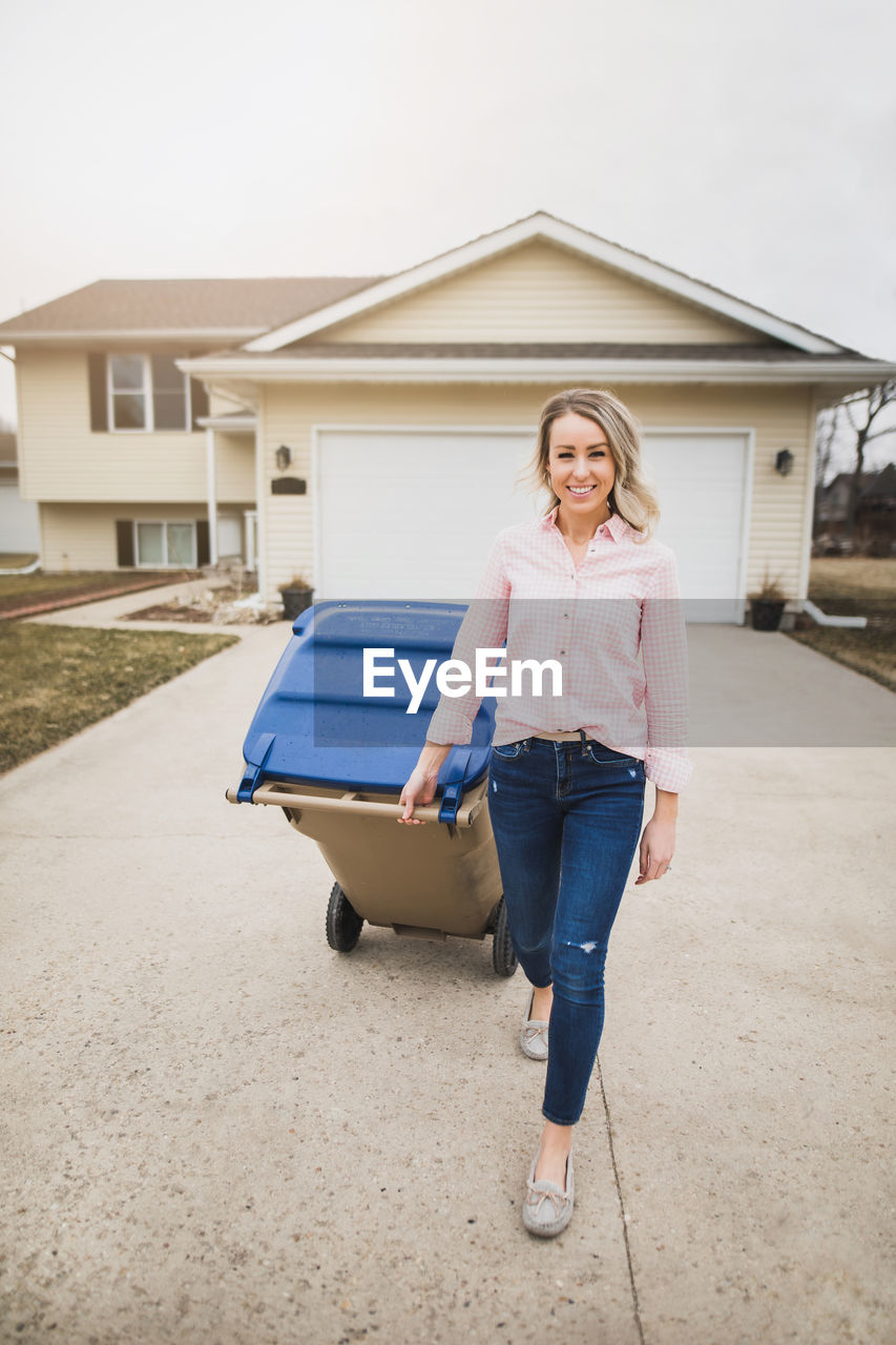 Portrait of woman with garbage bin walking on footpath