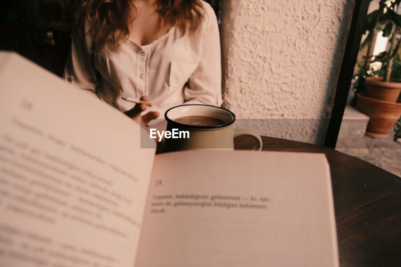 Book and coffee in front of woman smoking at home