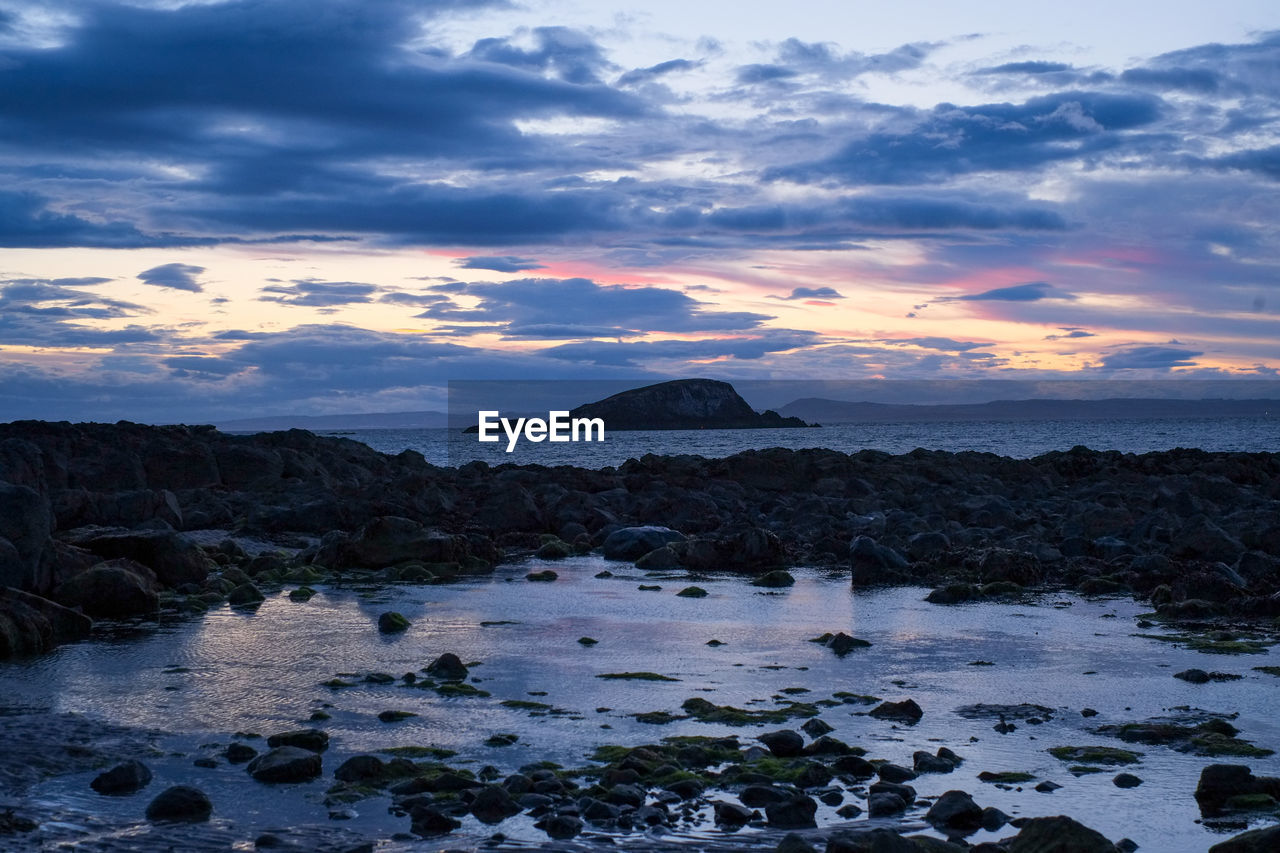 ROCKS ON SHORE AGAINST SKY DURING SUNSET