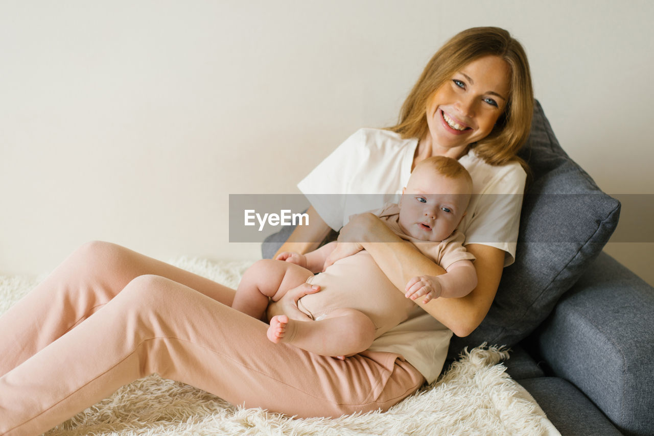 Loving mother holds her newborn baby in her arms at home, sitting on the couch