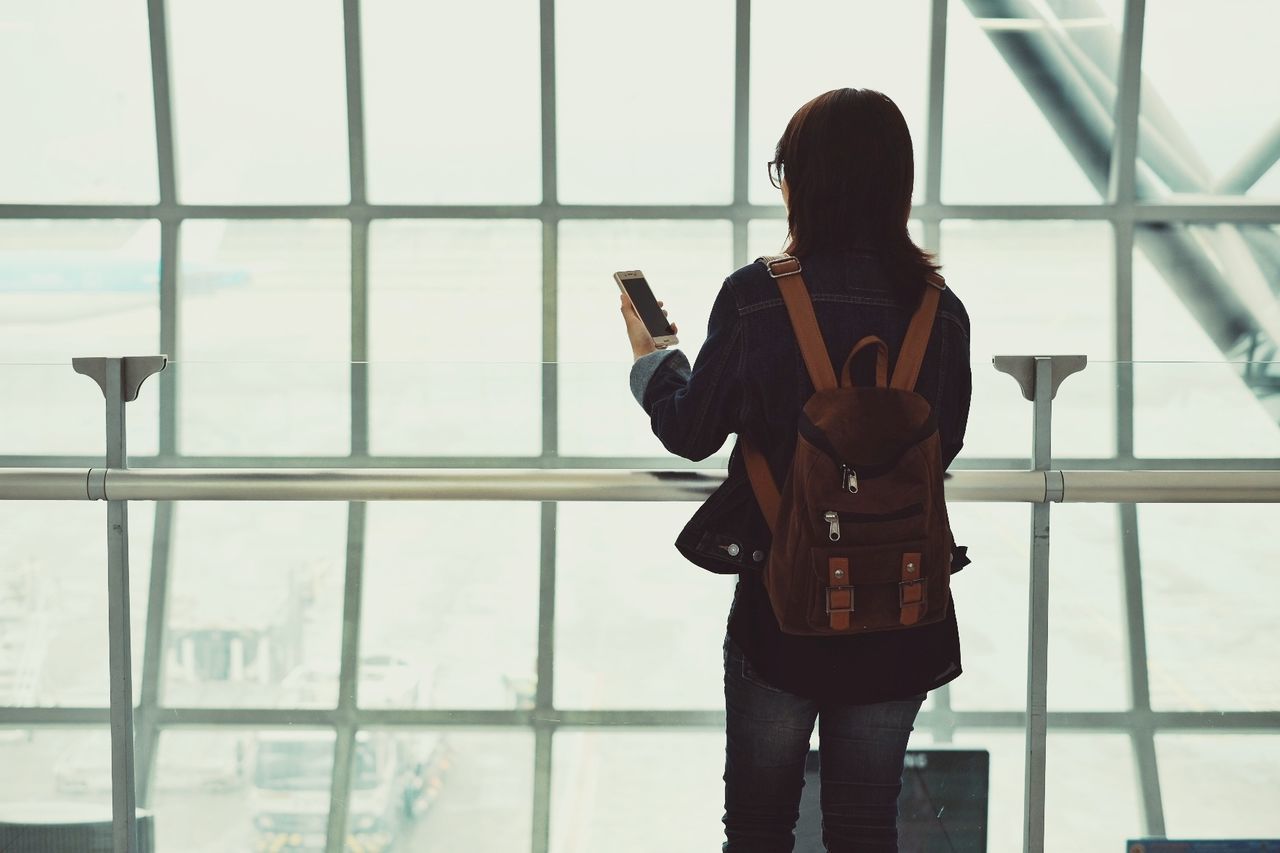 Rear view of woman using smart phone while standing on window