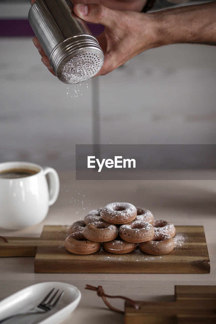 Cropped image of man dusting powdered sugar on donuts in kitchen