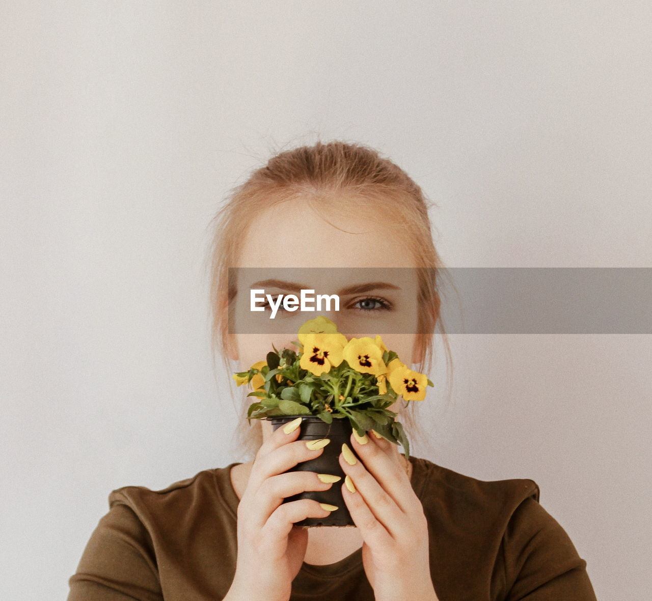 Portrait of young woman holding potted flowers against wall