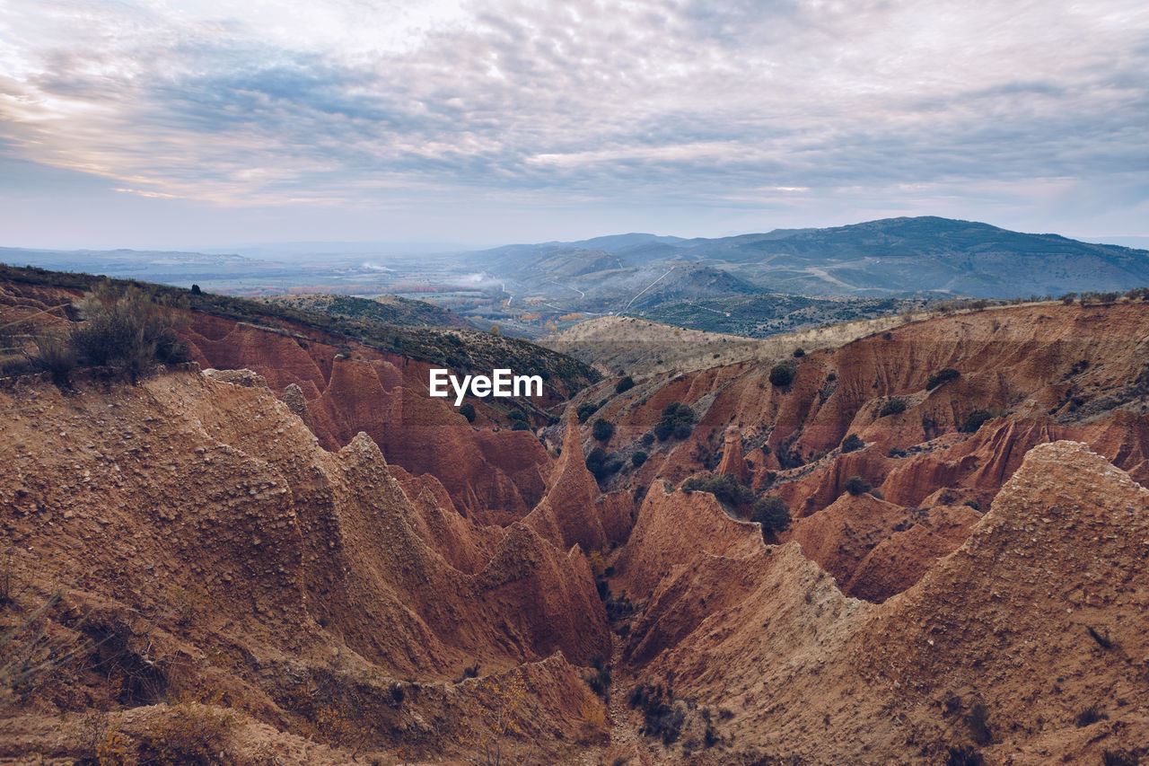 From above amazing landscape of sandstone rocky formations with uneven surface caused by erosion under blue cloudy sky in highlands