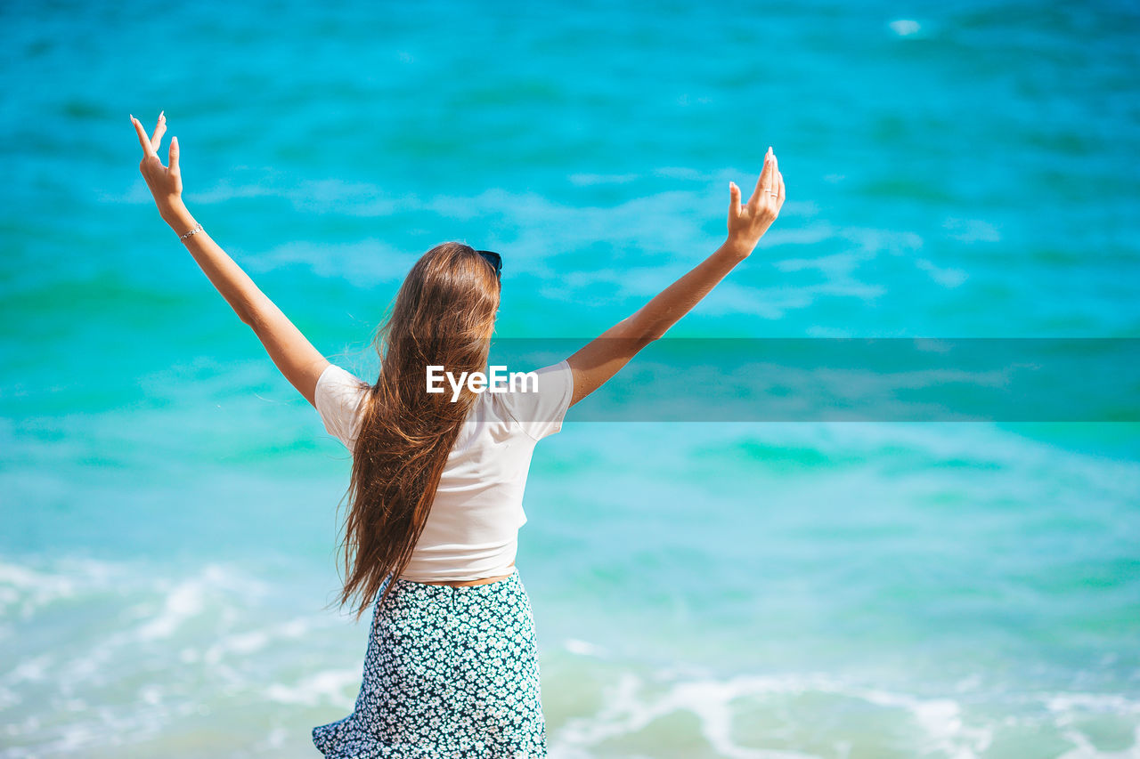 rear view of woman with arms raised standing on beach