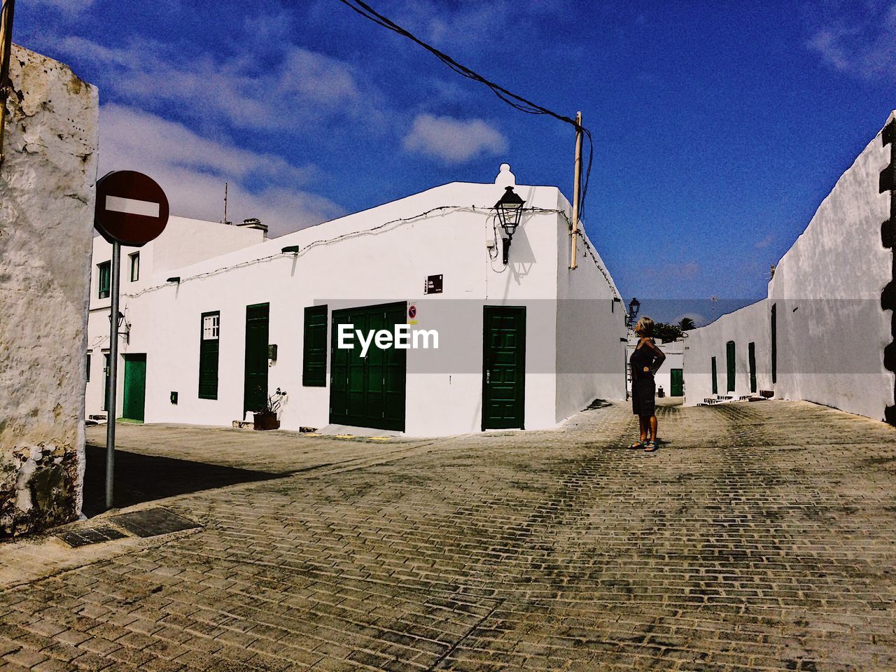 MAN WALKING ON FOOTPATH BY BUILDING AGAINST SKY