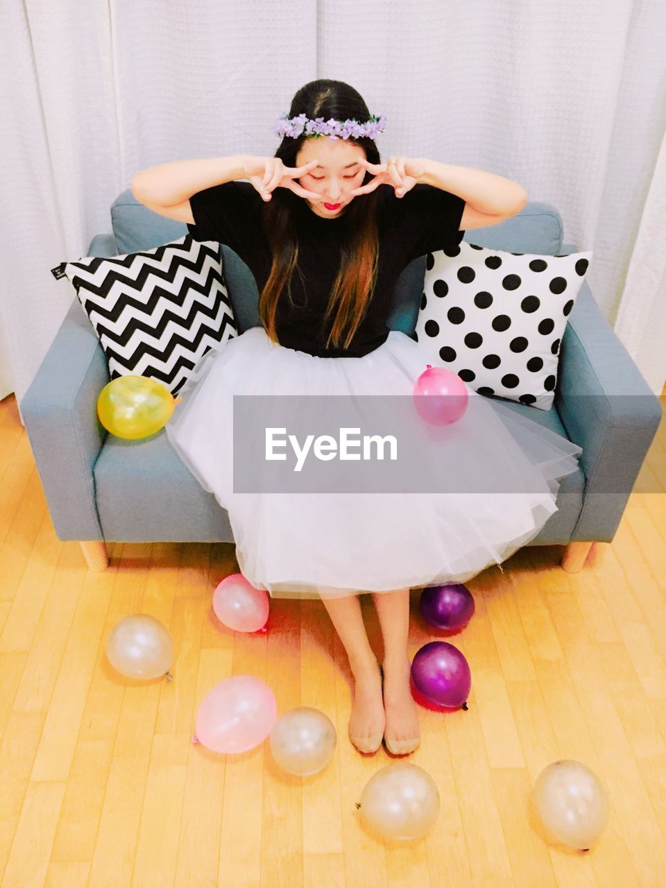 High angle view of woman gesturing while sitting on sofa amidst balloons at home
