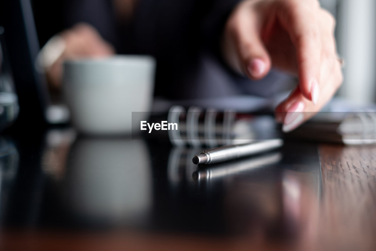 Close-up of businesswoman picking pen on table