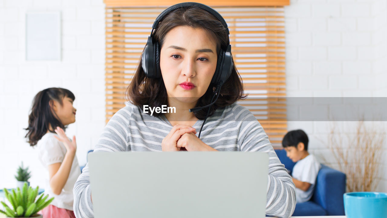 PORTRAIT OF A YOUNG WOMAN USING PHONE WHILE SITTING ON LAPTOP