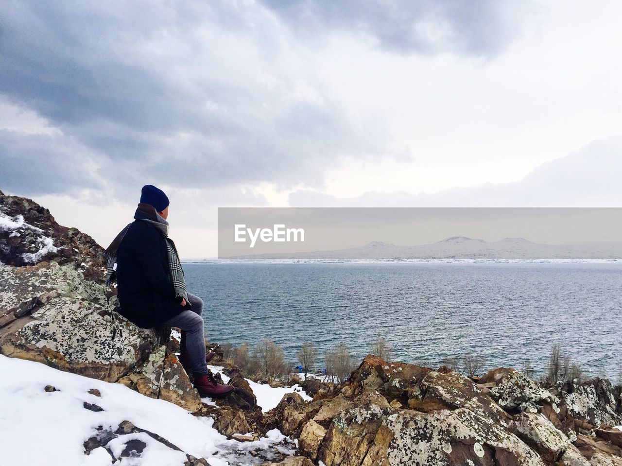 Side view of man sitting on rocks at beach against sky