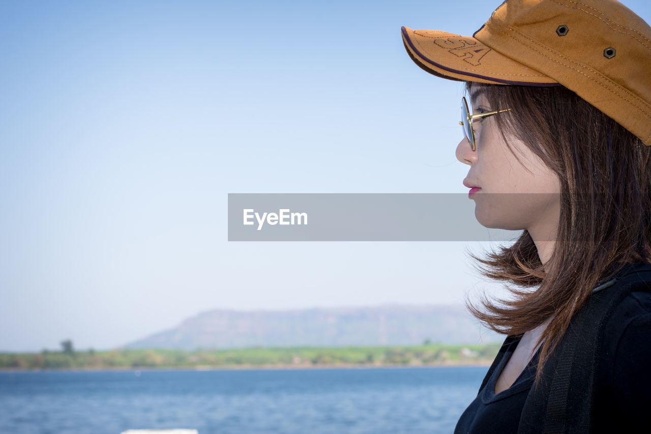 Side view of young woman by sea against sky