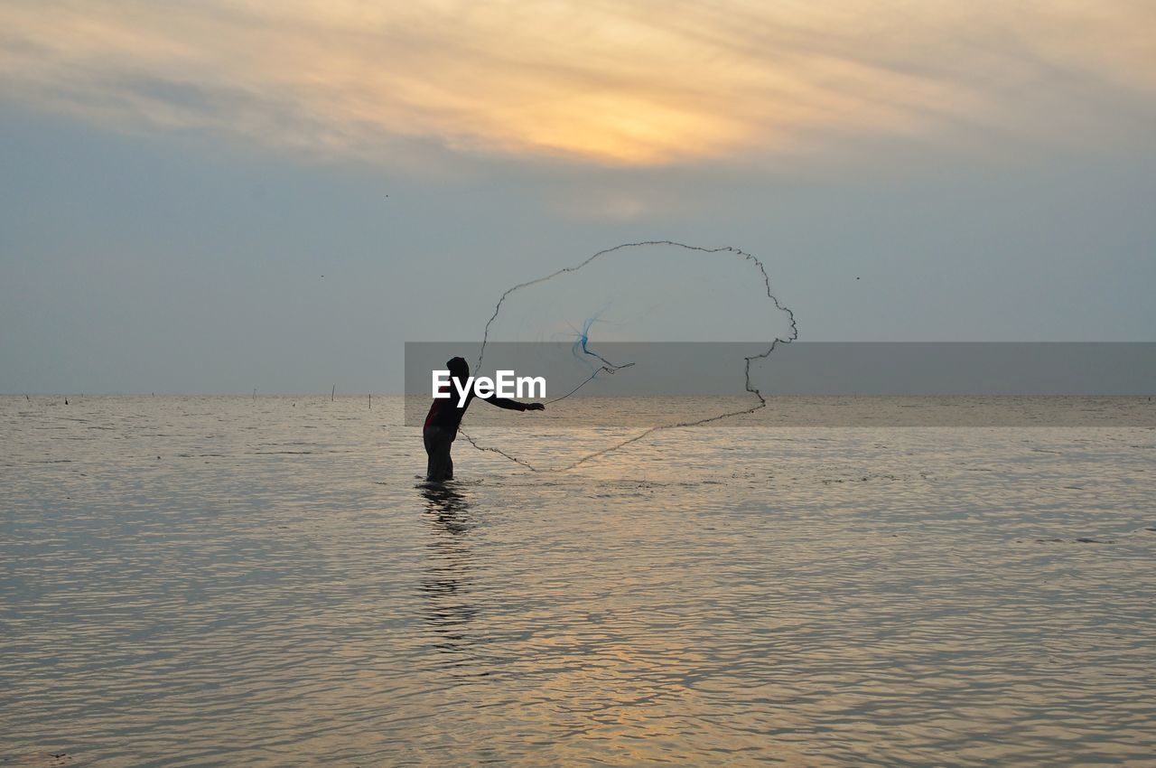 Silhouette young man fishing in sea against sky during sunset