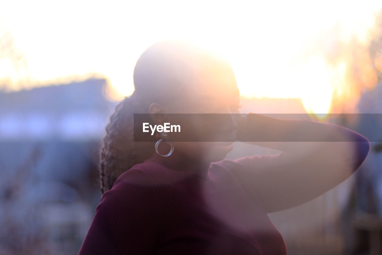 PORTRAIT OF WOMAN AGAINST SUN AT SUNSET