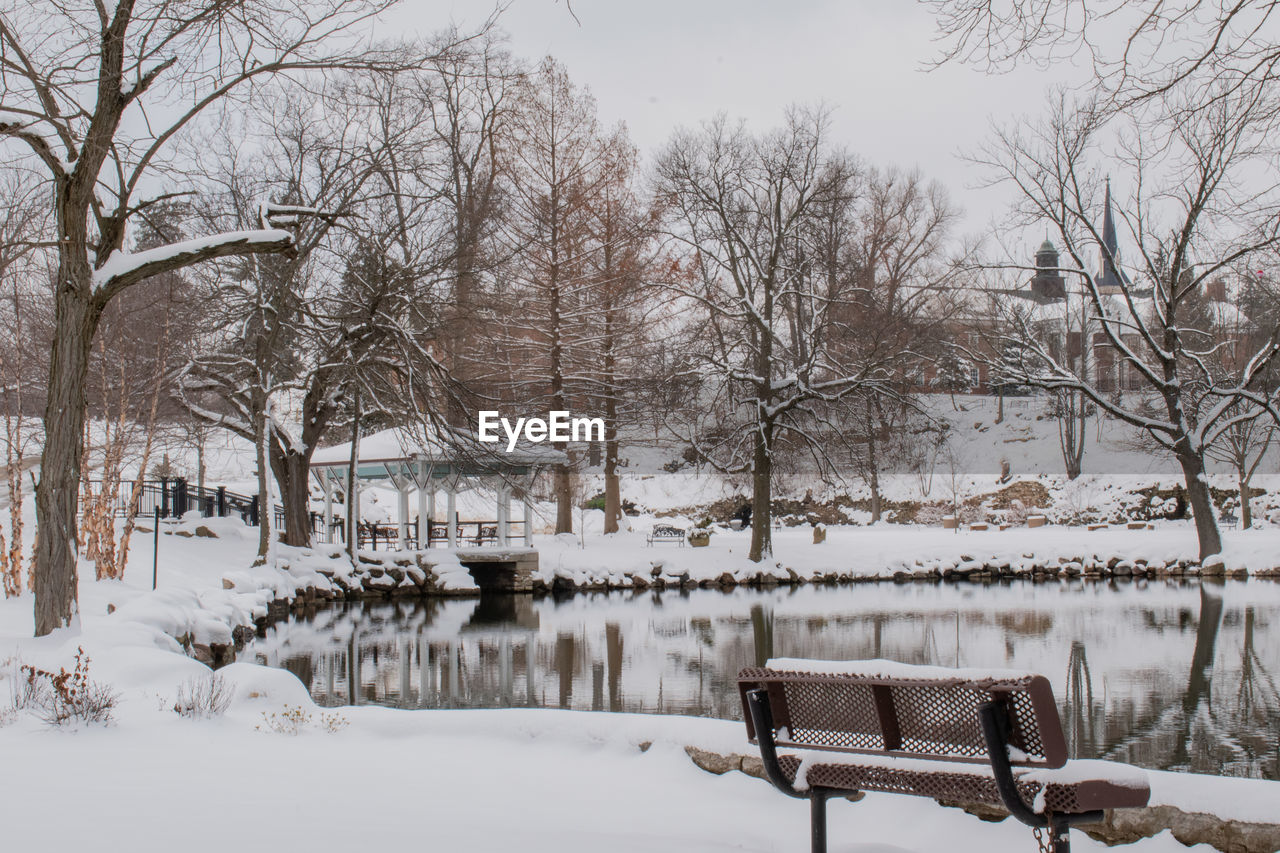 SNOW COVERED BARE TREES BY LAKE AGAINST SKY