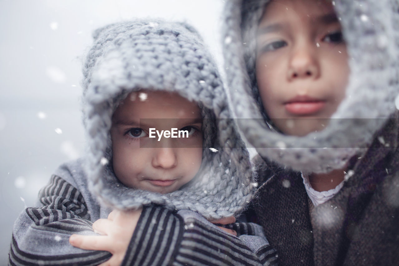 Girl in knitted grey hat hugging her frozen smaller brother