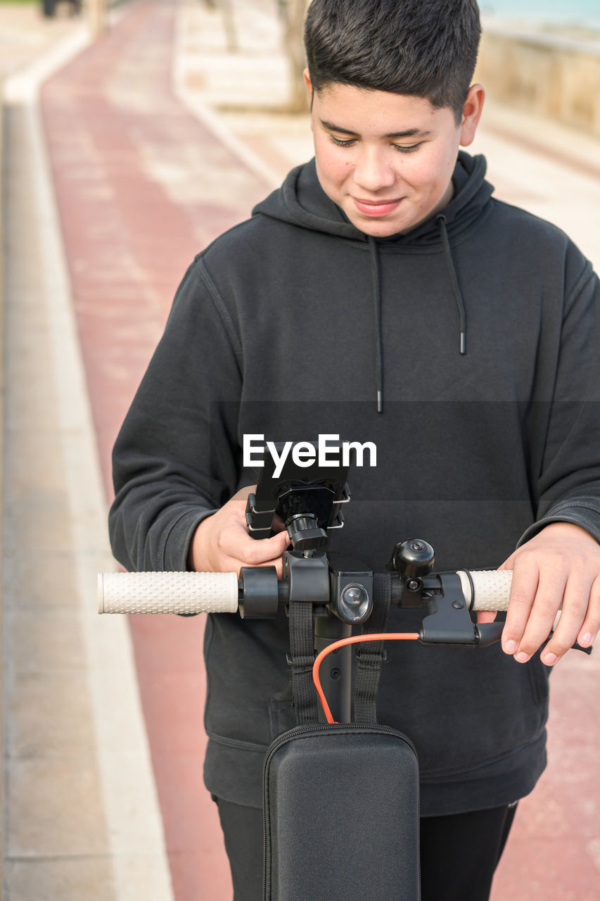 Smiling teenager riding an electric scooter using phone application e-mobility urban leisure concept