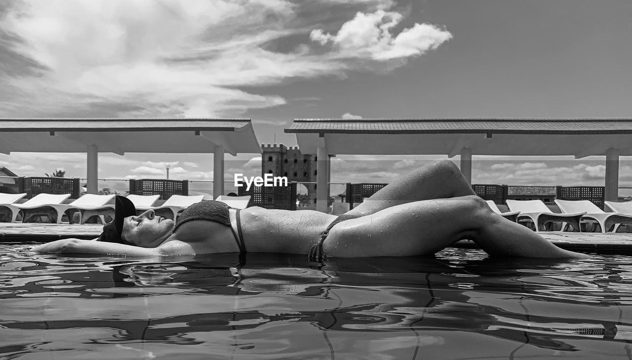 Side view of woman sitting on lounge chair against sky