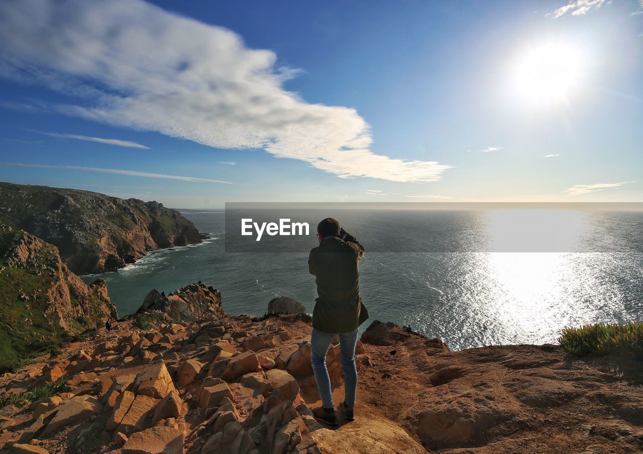 Rear view of man standing on rock against sea and sky