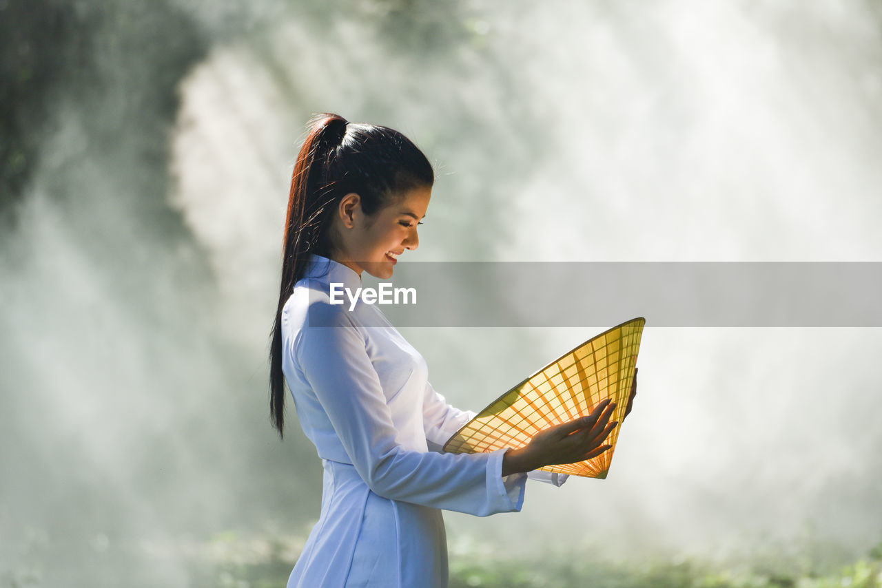 Side view of smiling young woman looking at asian style conical hat in village