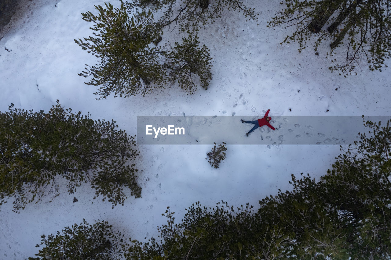 Drone aerial of woman wearing warm clothing lie down at fresh snow in winter