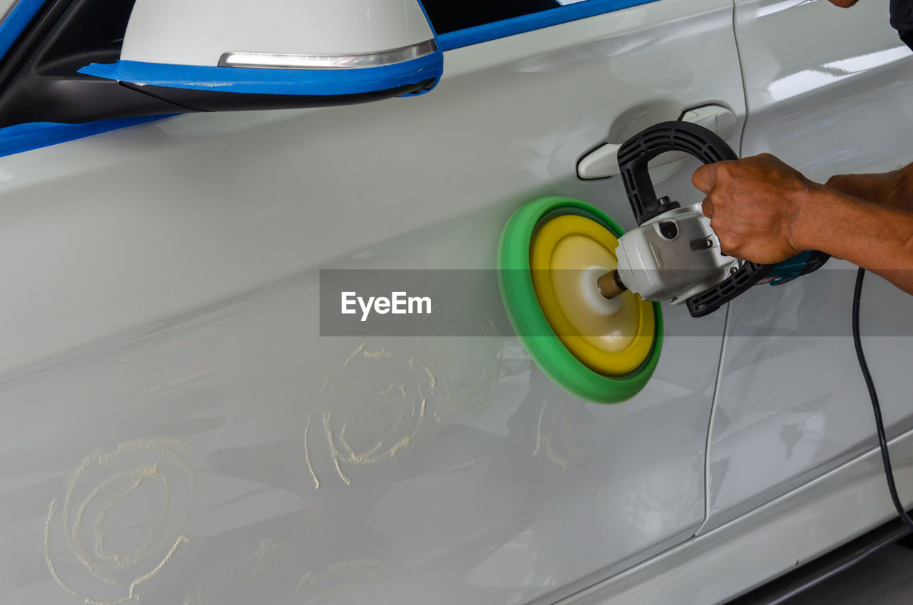 Cropped hands of mechanic polishing car in garage