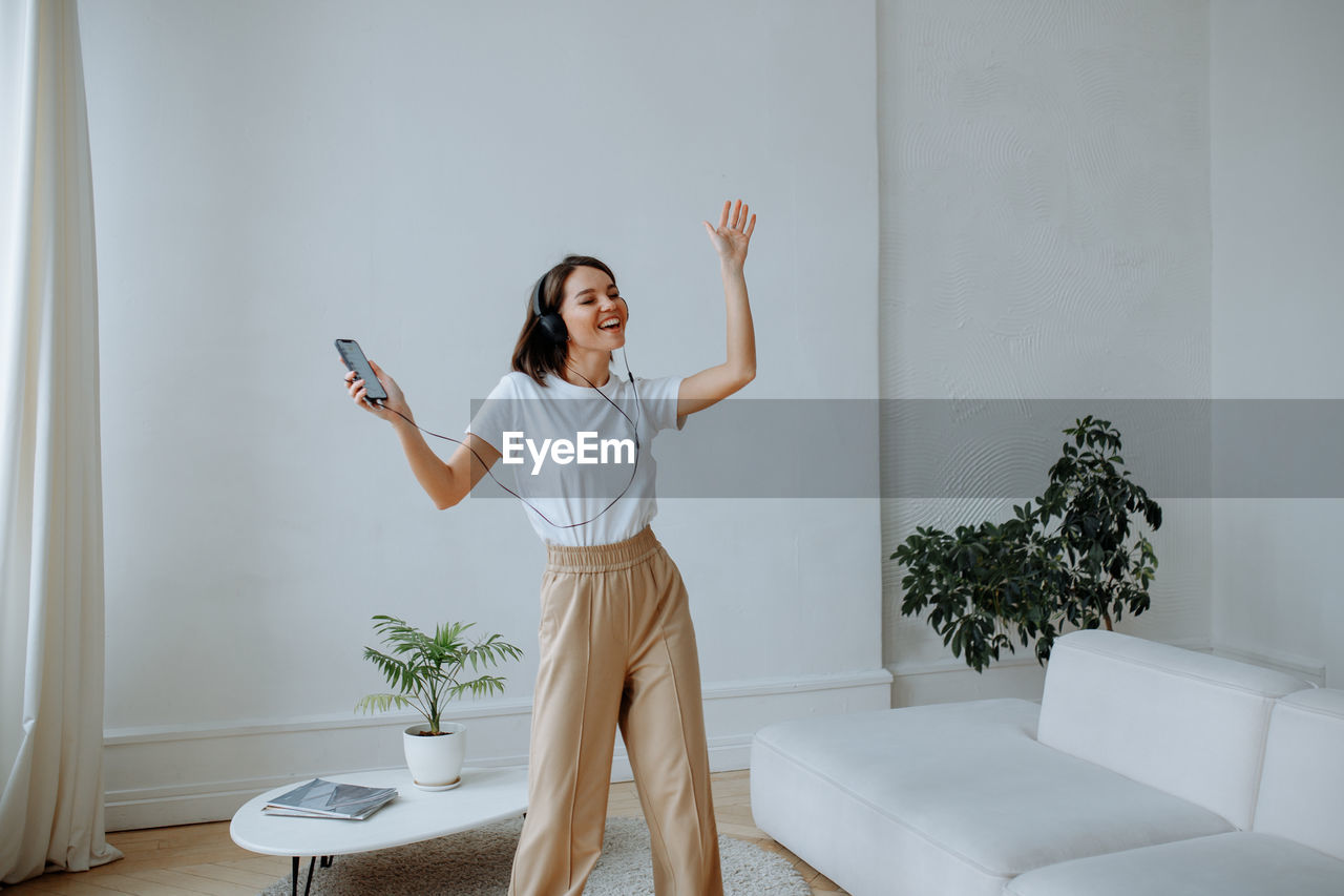 Young girl at home listening to music with headphones and dancing