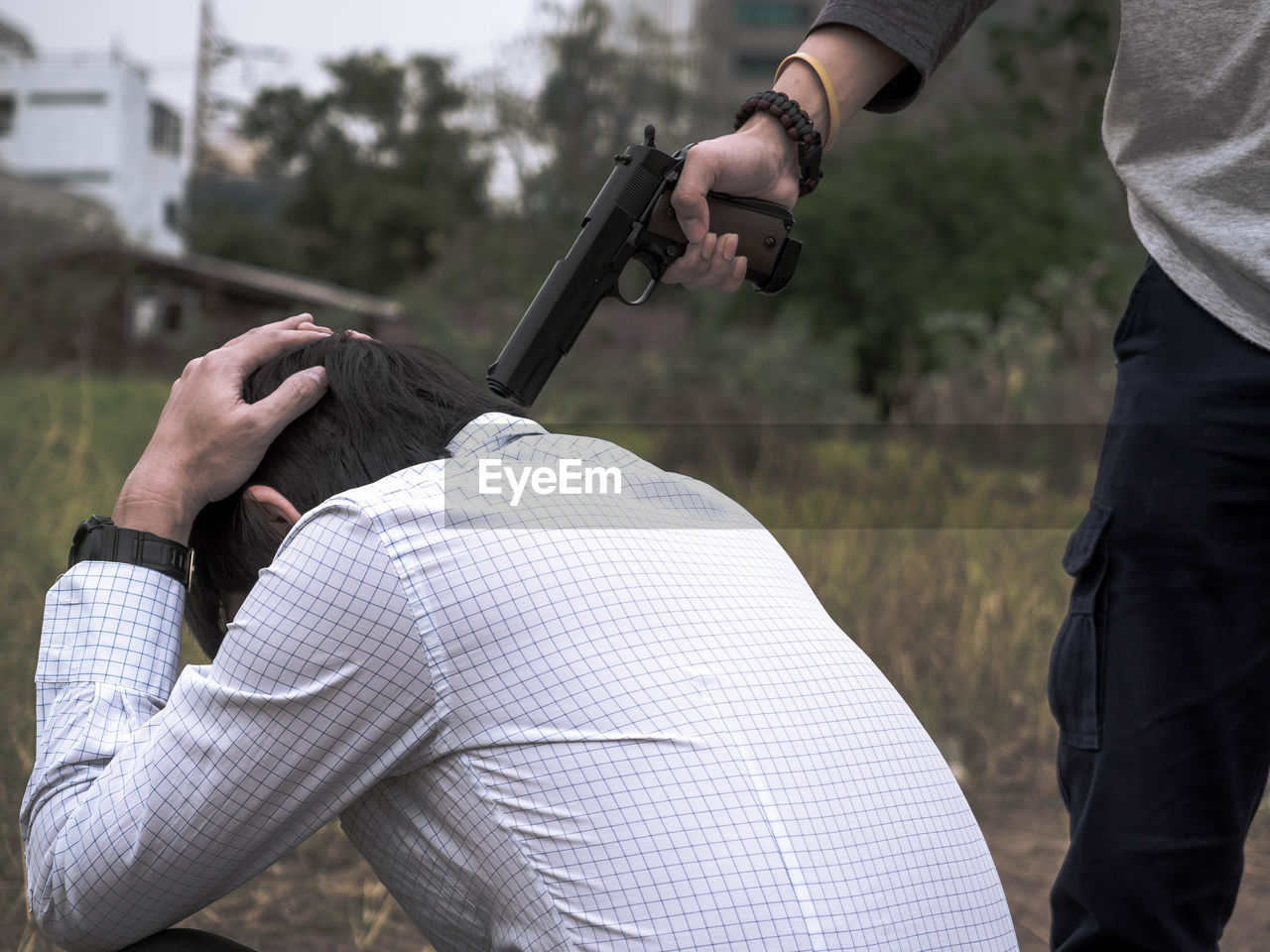 Midsection of thief aiming gun at man on field