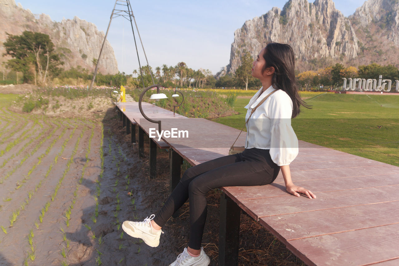 SIDE VIEW OF YOUNG WOMAN SITTING BY WATER